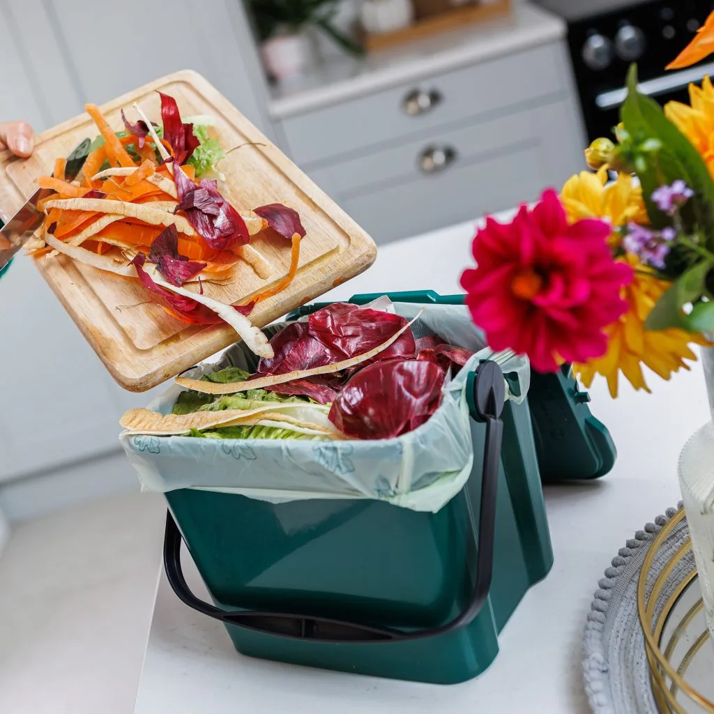 someone putting organic vegetable waste in a green food waste compostable bin